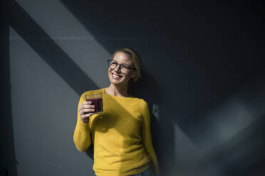 Woman in yellow pullover, holding glass of tea, enjoying the sun - JOSF03407