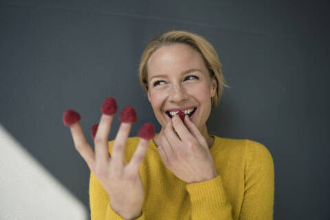 Blonde Frau mit Himbeeren an ihren Fingern, lachend, lizenzfreies Stockfoto