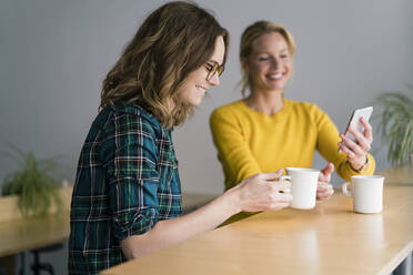 Zwei Freundinnen sitzen in einem Café, trinken Kaffee und benutzen ihr Smartphone - JOSF03417