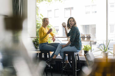Zwei Freundinnen sitzen in einem Café, haben Spaß und trinken Kaffee - JOSF03419