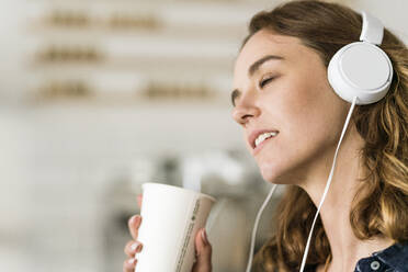Junge Frau in einem Café, die mit Kopfhörern Musik hört - JOSF03446