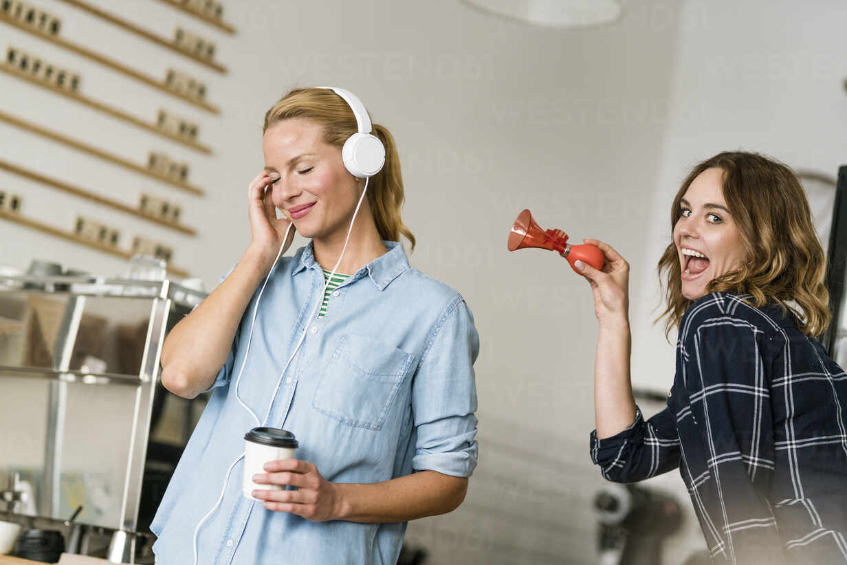 Frau im Café, die Musik hört, Freund versucht sie mit einer Hupe zu  unterbrechen, lizenzfreies Stockfoto