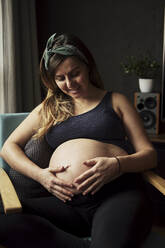 Schwangere Frau schaut auf ihren Babybauch zu Hause - BZF00484