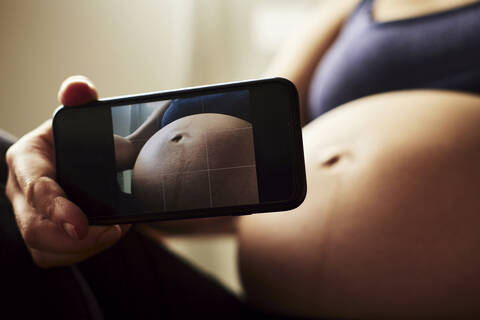 Schwangere Frau beim Fotografieren ihres Babybauchs, lizenzfreies Stockfoto