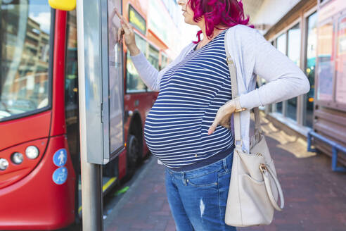 Pregnant woman at bus stop checking timetable - WPEF01573