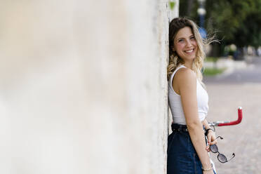 Portrait of happy young woman with sunglasses leaning against wall - GIOF06559