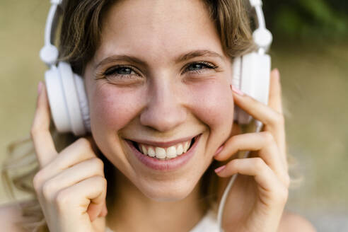 Porträt einer glücklichen jungen Frau, die mit Kopfhörern Musik hört - GIOF06572