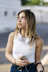 Portrait of young woman with headphones and smartphone looking up - GIOF06580