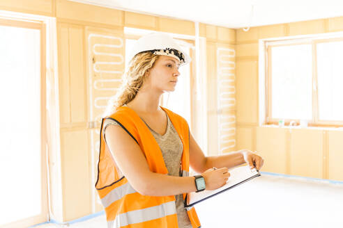 Junge Frau, die den Bau eines neuen Holzhauses kontrolliert - TCF06139