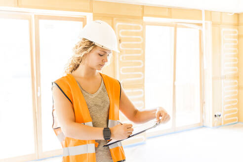 Junge Frau, die den Bau eines neuen Holzhauses kontrolliert - TCF06140