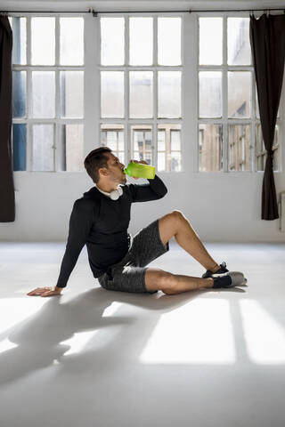 Sportler macht eine Pause im sonnigen Studio und trinkt Wasser, lizenzfreies Stockfoto