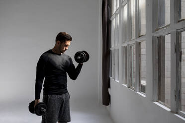 Handsome man doing workout in his loft studio with dumbbells - MAUF02645