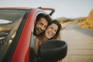 Glückliches Paar auf einer Autoreise mit Blick aus dem Autofenster - DMGF00079