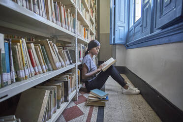 Junge Frau sitzt auf dem Boden und liest ein Buch in der Nationalbibliothek, Maputo, Mocambique - VEGF00393