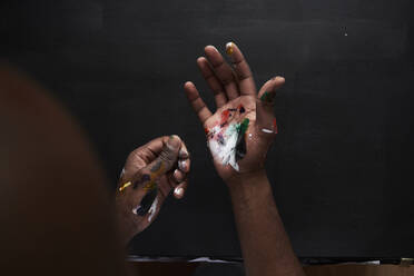 Dirty hands of artist with colorful paints against black background - IGGF01241