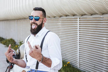 Portrait of motorcyclist with mirrored sunglasses giving the finger while sticking out tongue - LJF00285