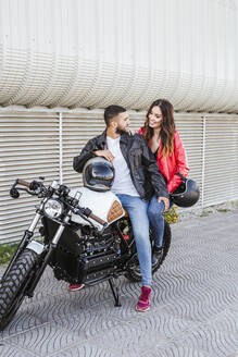 Glückliches Paar mit Motorradhelmen auf einem Motorrad sitzend - LJF00290