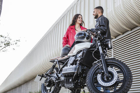 Pärchen mit Motorradhelmen steht neben einem Motorrad, lizenzfreies Stockfoto