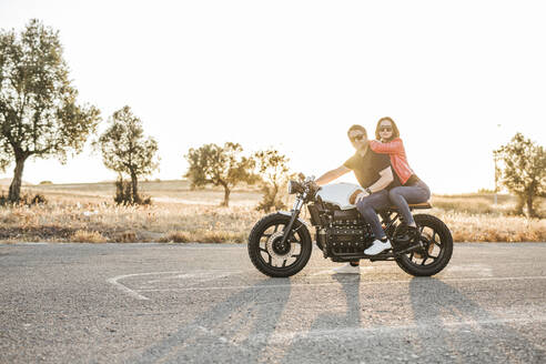 Porträt eines Paares auf einem Motorrad sitzend in der Abenddämmerung - LJF00310