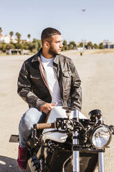 Porträt eines bärtigen jungen Mannes, der auf seinem Motorrad sitzt - LJF00313