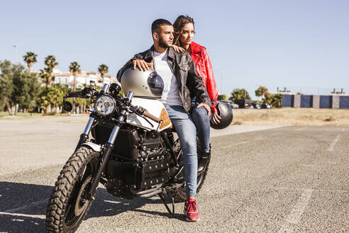 Paar sitzt auf einem Motorrad und schaut in die Ferne - LJF00317