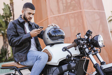 Junger Mann sitzt auf seinem Motorrad und benutzt ein Mobiltelefon - LJF00326