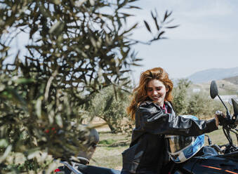 Porträt einer fröhlichen rothaarigen Frau auf einem Motorrad, Andalusien, Spanien - LJF00333