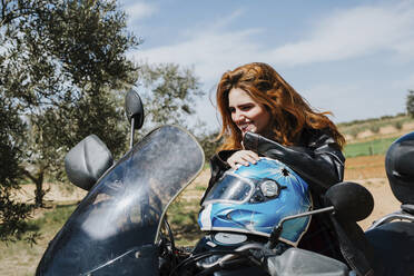 Porträt einer fröhlichen rothaarigen Frau auf einem Motorrad, Andalusien, Spanien - LJF00336