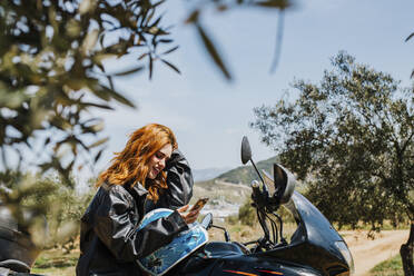 Rothaarige Frau auf Motorrad schaut auf Handy, Andalusien, Spanien - LJF00340