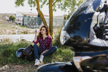 Motorcyclist having cigarette break under a tree - LJF00347