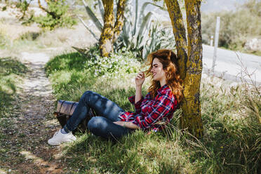 Redheaded woman having cigarette break under a tree - LJF00350