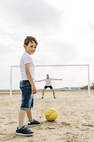 Mann und Junge spielen Fußball am Strand, lizenzfreies Stockfoto