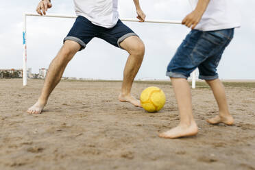 Legs of boy and man playing soccer on the beach - JRFF03429