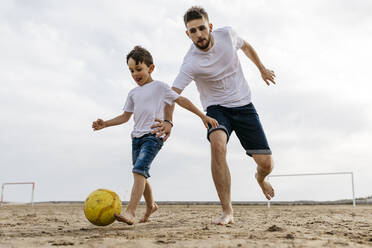 Boy and man playing soccer on the beach - JRFF03430