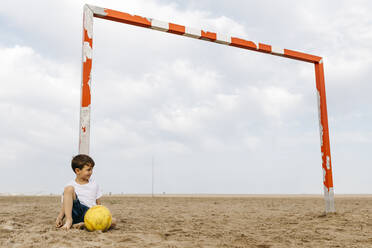 Boy sitting on the beach and leaning against soccer goal - JRFF03432