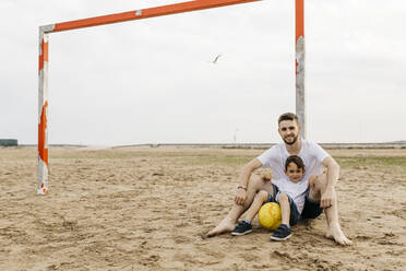Mann und Junge ruhen sich nach einem Fußballspiel am Strand aus - JRFF03436