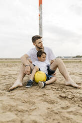 Mann und Junge ruhen sich nach einem Fußballspiel am Strand aus - JRFF03437