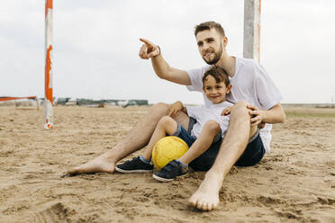 Man and boy resting after soccer game on the beach - JRFF03438