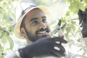 Portrait of bearded young man pruning twigs of tree - SGF02380