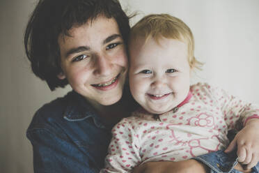 Portrait of happy teenage boy hugging his toddler sister - IHF00166