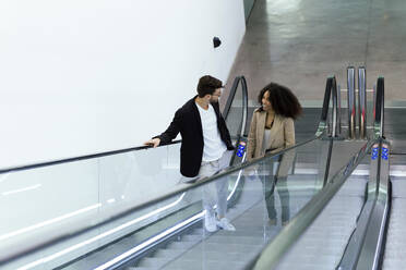 Zwei junge Geschäftspartner unterhalten sich auf einer Rolltreppe - JSRF00374