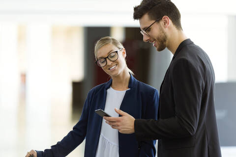 Zwei lächelnde junge Geschäftspartner, die ein Smartphone benutzen, lizenzfreies Stockfoto