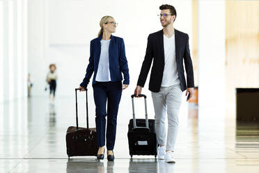 Zwei lächelnde junge Geschäftspartner beim Spaziergang auf dem Flughafen - JSRF00380