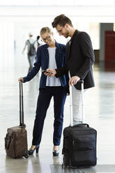 Two smiling young business partners using a smartphone at the airport - JSRF00381