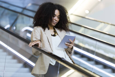 Young businesswoman using a tablet on an escalator stock photo