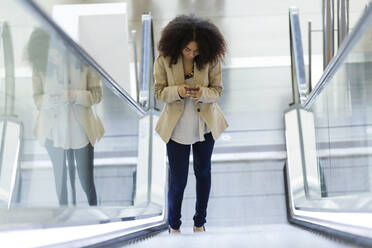 Junge Geschäftsfrau benutzt ein Smartphone auf einer Rolltreppe - JSRF00399