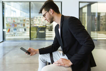 Young businessman sitting on a bench using a smartphone - JSRF00403