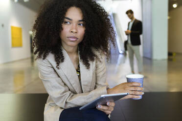 Young businesswoman with takeaway coffee and tablet in a foyer - JSRF00406