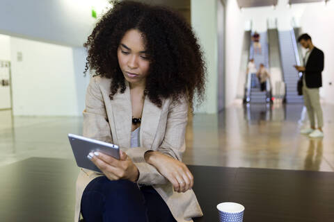 Junge Geschäftsfrau mit Kaffee zum Mitnehmen und Tablet in einem Foyer, lizenzfreies Stockfoto