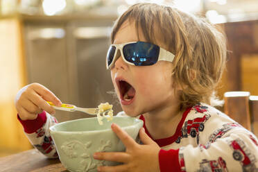 Kaukasischer Junge mit Sonnenbrille beim Essen in der Küche - BLEF08238